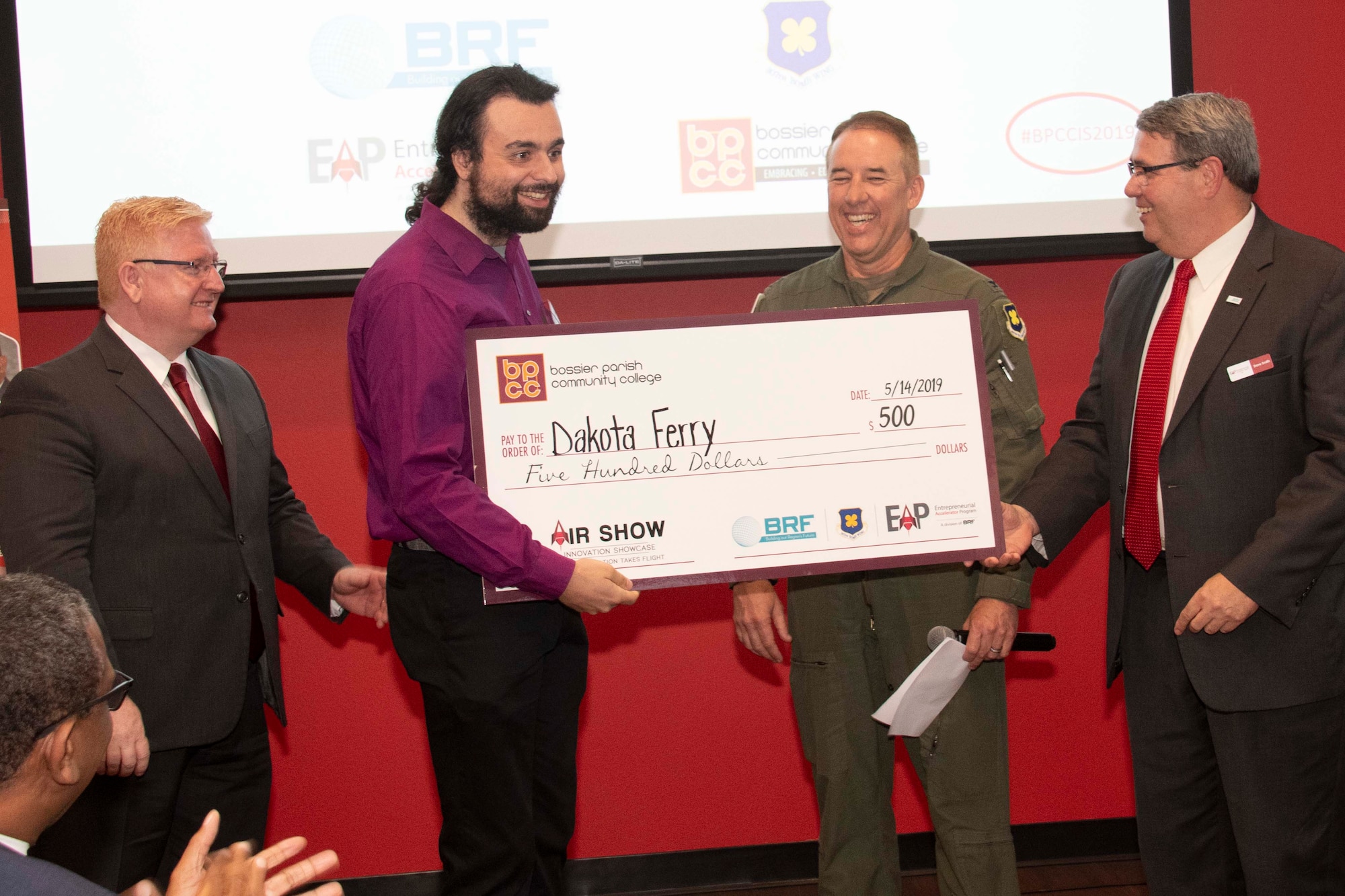 Dr. Rick Bateman,Jr., Bossier Parish Community College chancellor, U.S. Air Force Col. Steven Kirkpatrick, 307th Bomb Wing commander, and Dave Smith, Entrepreneurial Accelerator Program executive director, present Dakota Ferry with a check in Bossier City, La., May 14, 2019.  Ferry, a BPCC student, won first place in the 2-Minute Drill, a contest for budding entrepreneurs co-sponsored by the 307th Bomb Wing.  The presentation was part of the inaugural AirShow Innovation Showcase, an event highlight achievments of innovative business that utilized the EAP as a resource. (U.S. Air Force photo by Master Sgt. Ted Daigle )