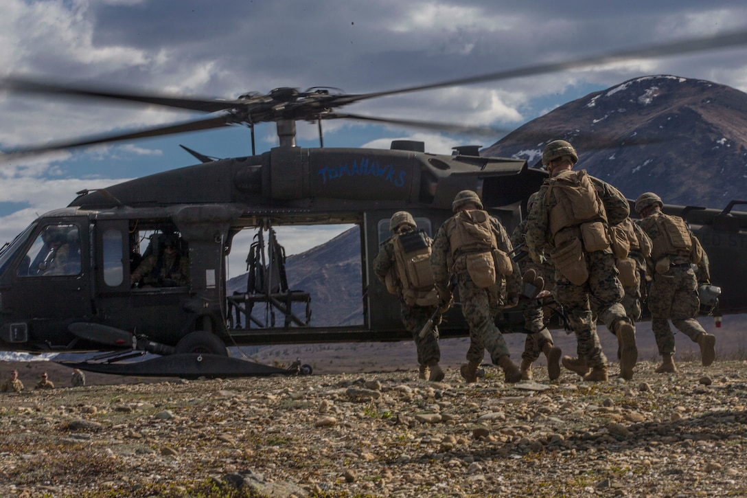 Marines run toward a helicopter.
