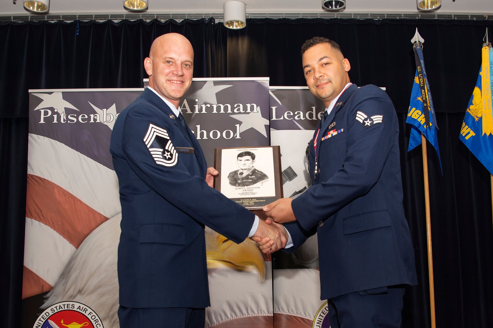 U.S. Air Force Chief Master Sgt. Christopher Ostrom, 52nd Civil Engineer Squadron fire chief, left, presents the John L. Levitow award to Senior Airman Justin Gray, 52nd Operations Support Squadron air traffic controller, right, during the Pitsenbarger Airman Leadership School 19-D graduation in Club Eifel at Spangdahlem Air Base, Germany, May 16, 2019. The Levitow award is the highest honor given to the student who displays excellence in all categories of ALS. (U.S. Air Force photo by Airman 1st Class Valerie Seelye)