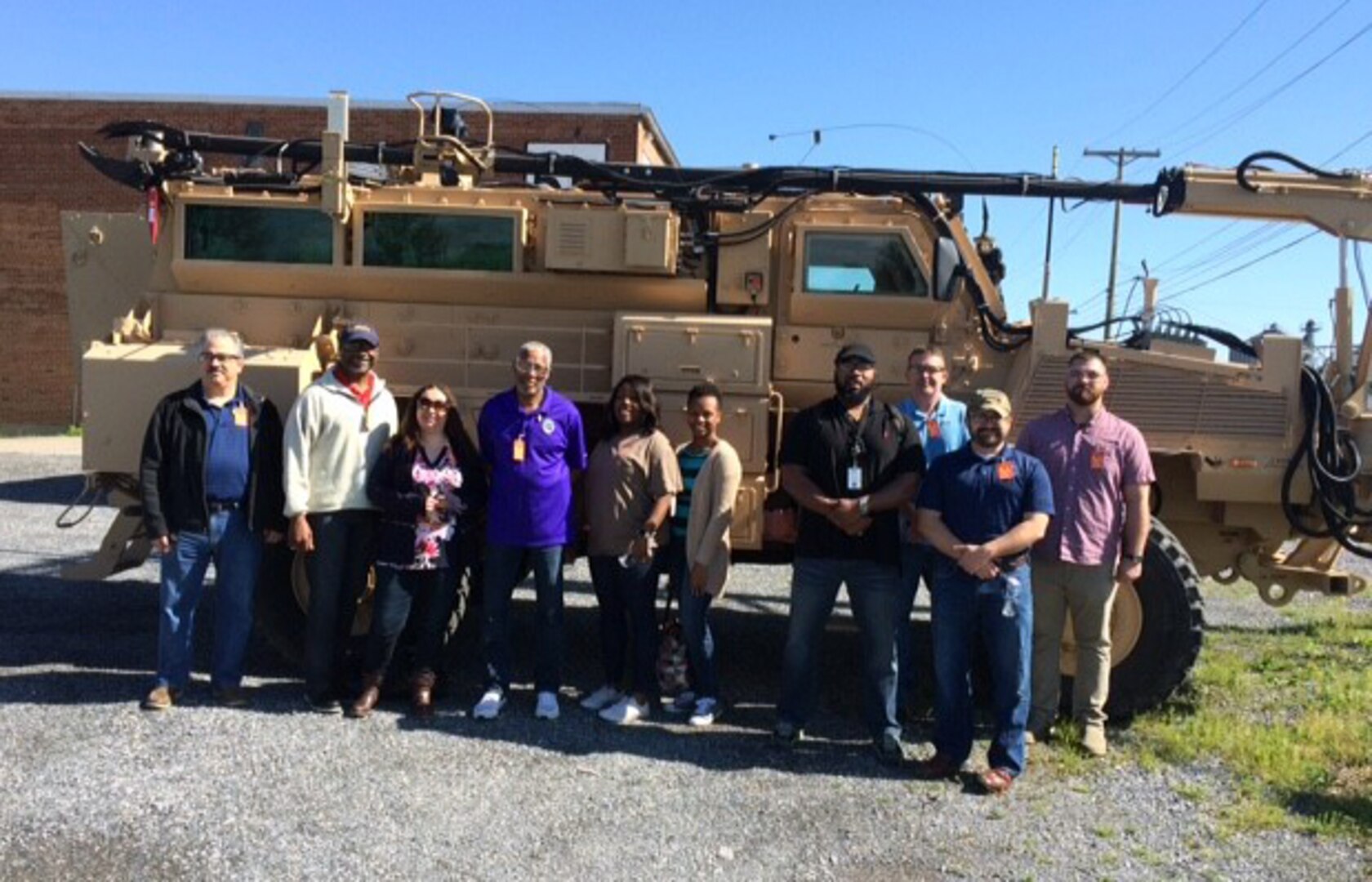 Group poses for a photograph in front of a Route Clearance Vehicle