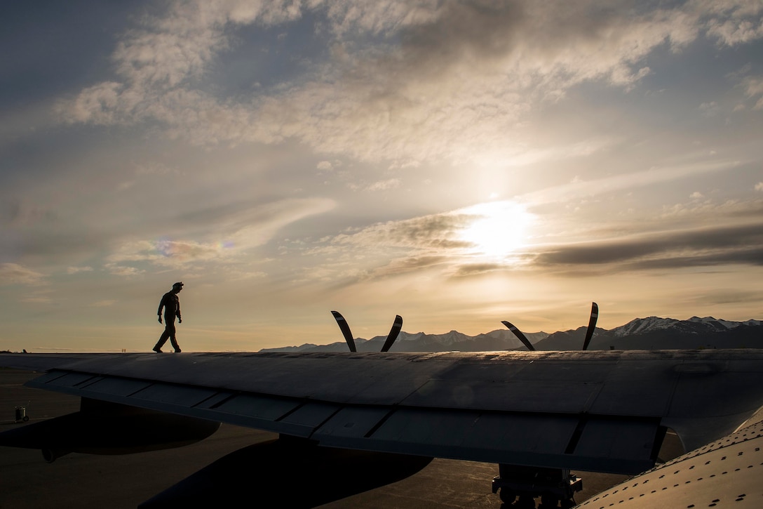 A silhouette of a man as he walks along the wing of a plane at twilight.