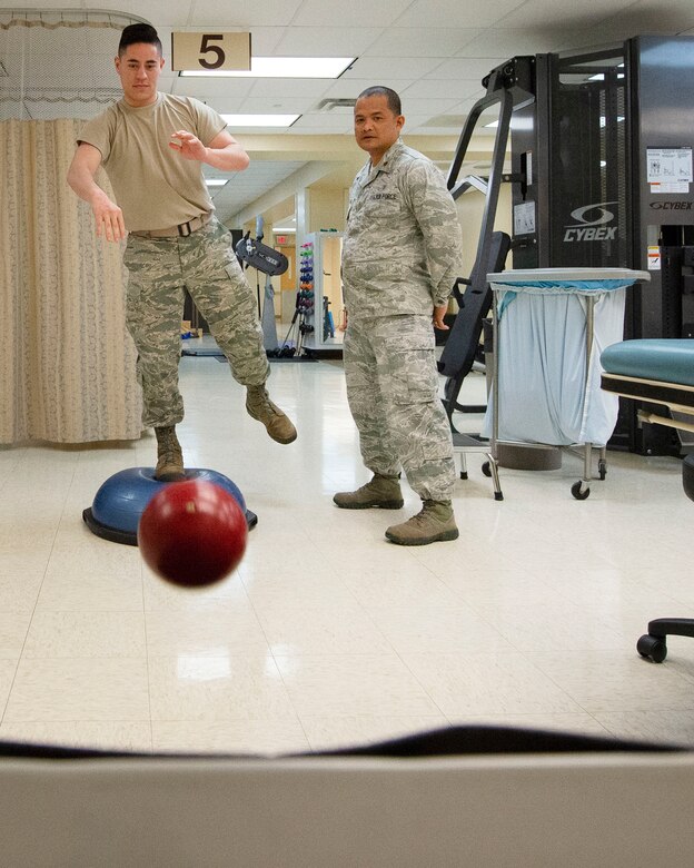 U.S. Air Force Maj. Karlo Mariano, 88th Medical Operations Squadron physical therapist, guides Senior Airman Aaron Perry, 88th MDOS physical medicine technician on the BOSU, which works proprioception, sense of balance inside the Physical Medicine Flight, Wright –Patterson Air Force Base Medical Center, Ohio, April 8, 2019. Mariano tailors workouts for clients to help with faster recovery from injuries.