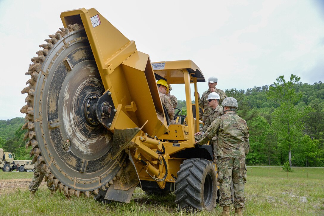 Soldiers and airmen use a large saw to drill into the ground.