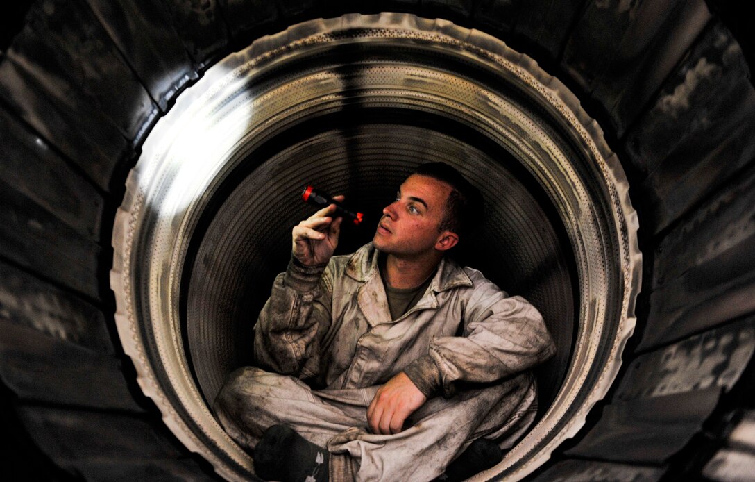 An airman holds a flashlight as he inspects the inside of a military jet.