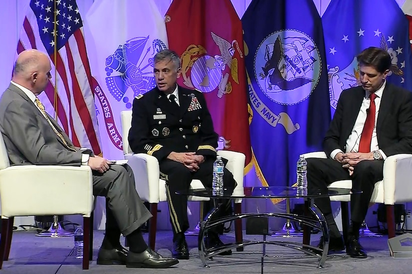 Three men sit in chairs around a small table.