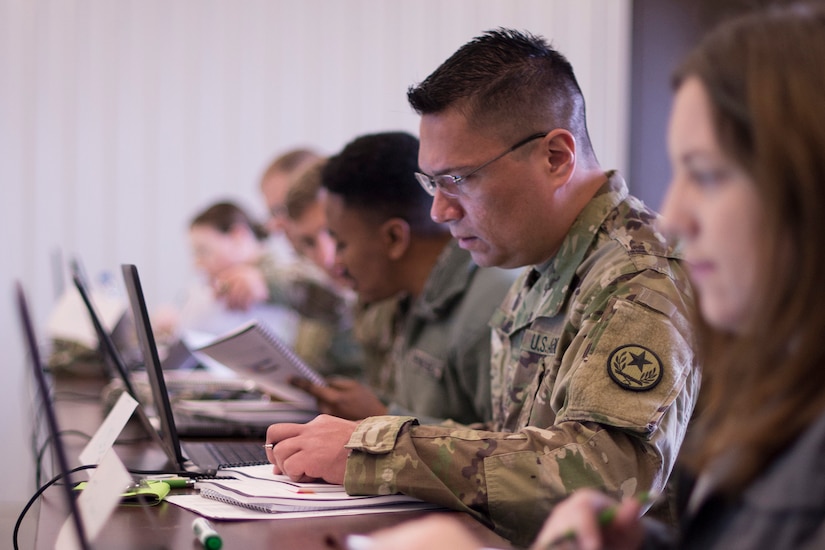 Service members and civilians sit at computers.
