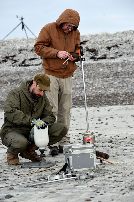 Two men hook up a device on a barren landscape.