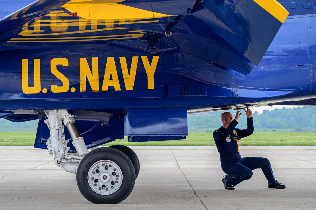 A crouching sailor checks the underside of a fighter jet.