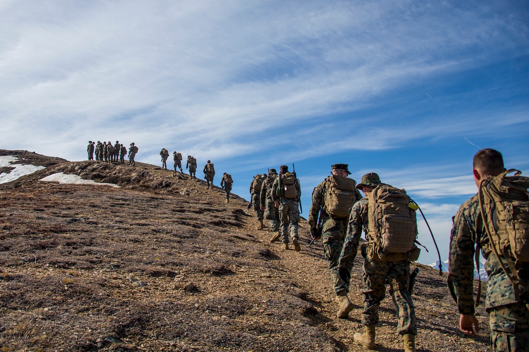 A group of Marines hike up a mountain.