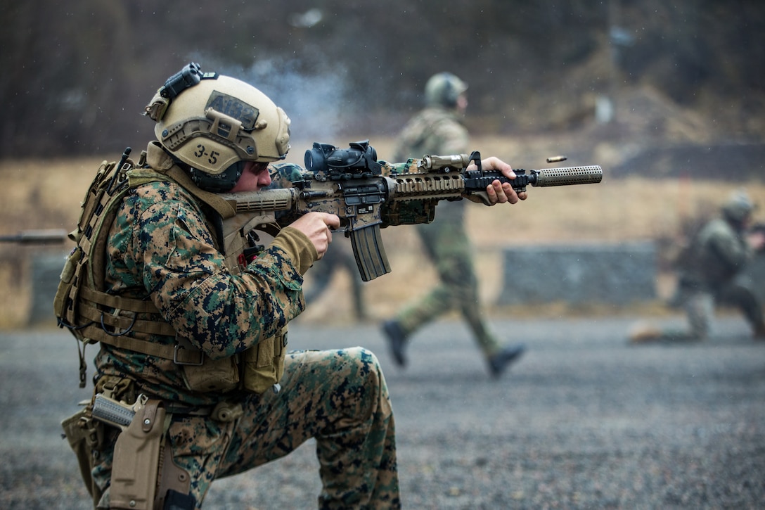 A Marine fires a rifle as other Marines run toward the target.