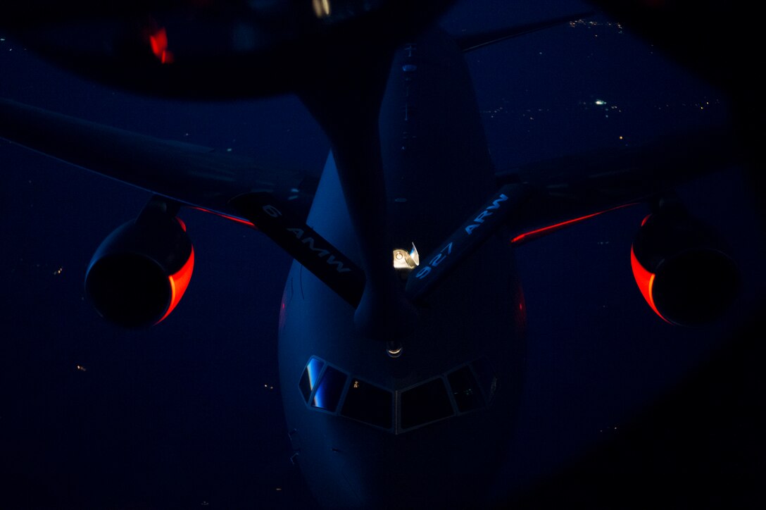 A refueling probe descends toward an aircraft in midair at night.