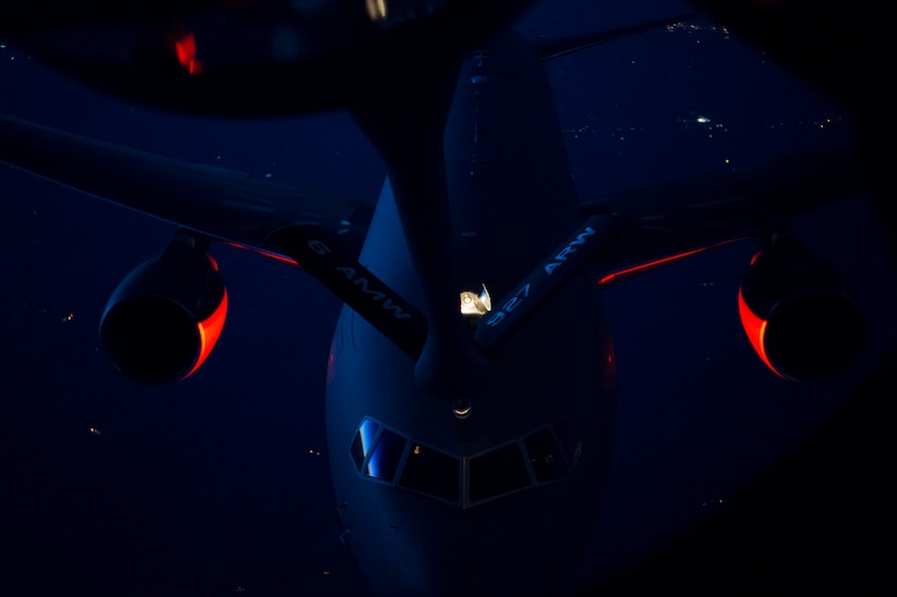 A refueling probe descends toward an aircraft in midair at night.