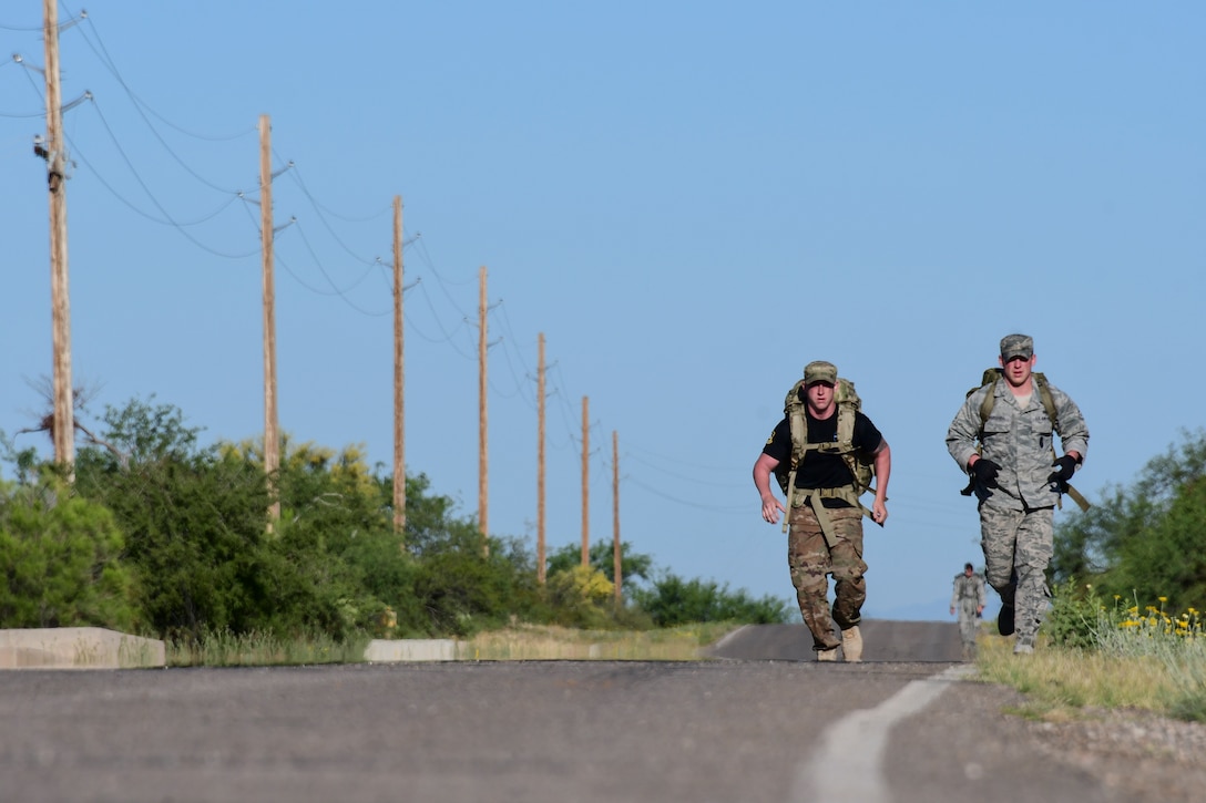 Airmen carrying backpacks march along a road.