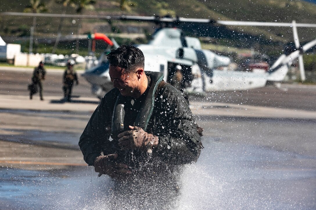 A Marine reacts to a spay of water with an aircraft in the background.