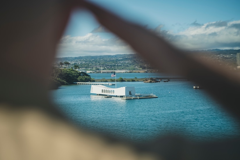 The USS Arizona memorial is seen through the saluting hand of a Marine.