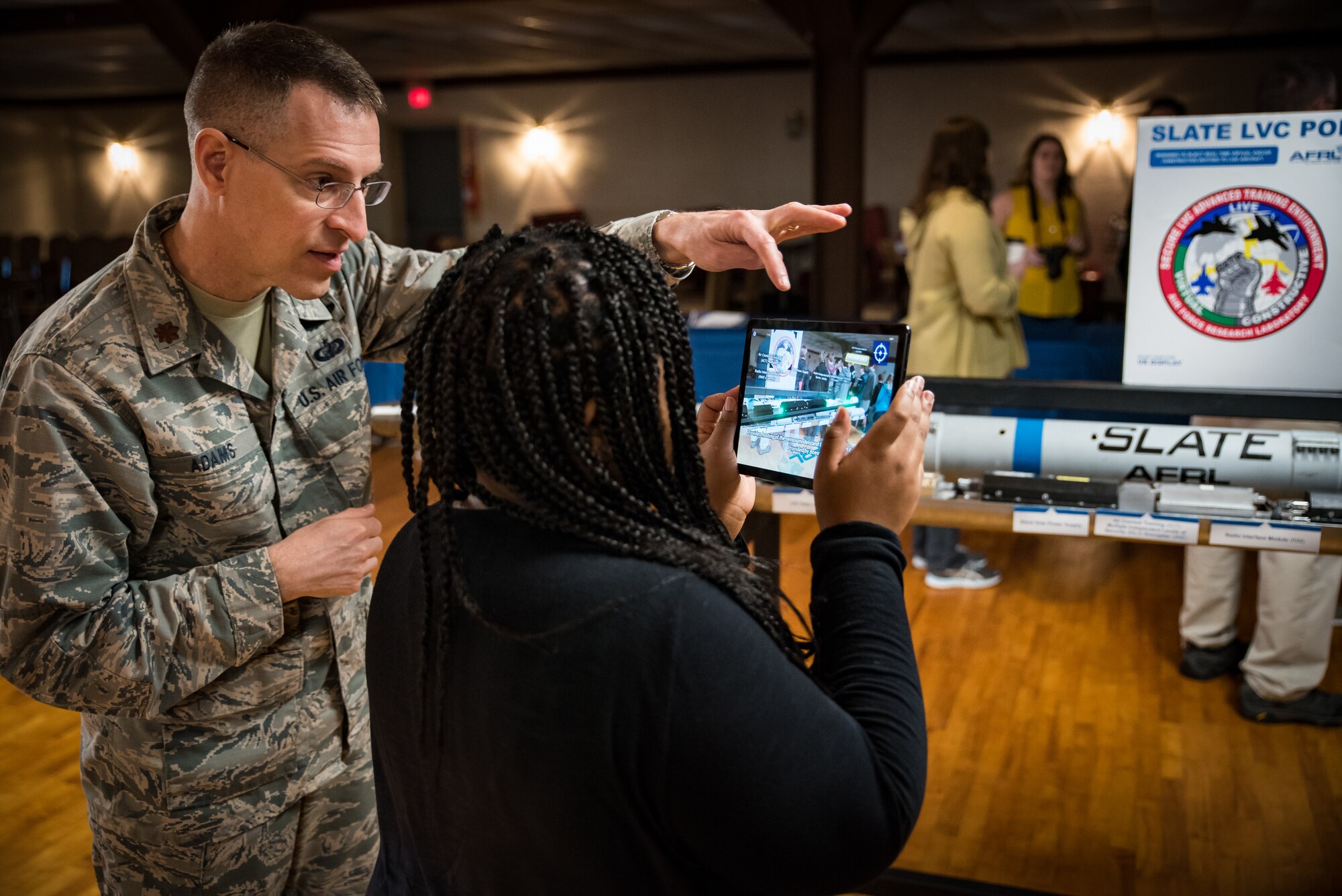 Using augmented reality and a tablet, Maj. Thomas Adams shows a participant how the components of the SLATE pod communicate with a live pilot to enhance live, virtual and constructive training during the Air Force Research Laboratory’s 7th annual Full Throttle STEM at Eldora Speedway May 14. (U.S. Air Force photo/Richard Eldridge)
