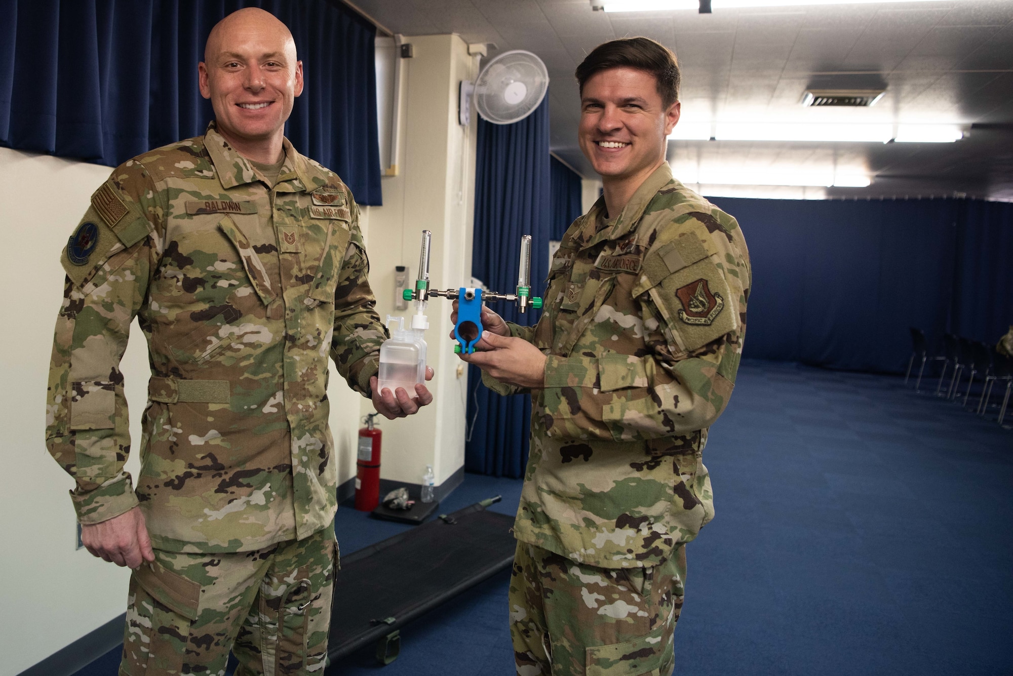 U.S. Air Force Staff Sgt. Dylan King and Tech. Sgt. Christian Baldwin, 18th Aeromedical Evacuation Squadron medical technicians, pose with their medical bottle handle invention, May.10, 2019, at Kadena Air Base, Japan.