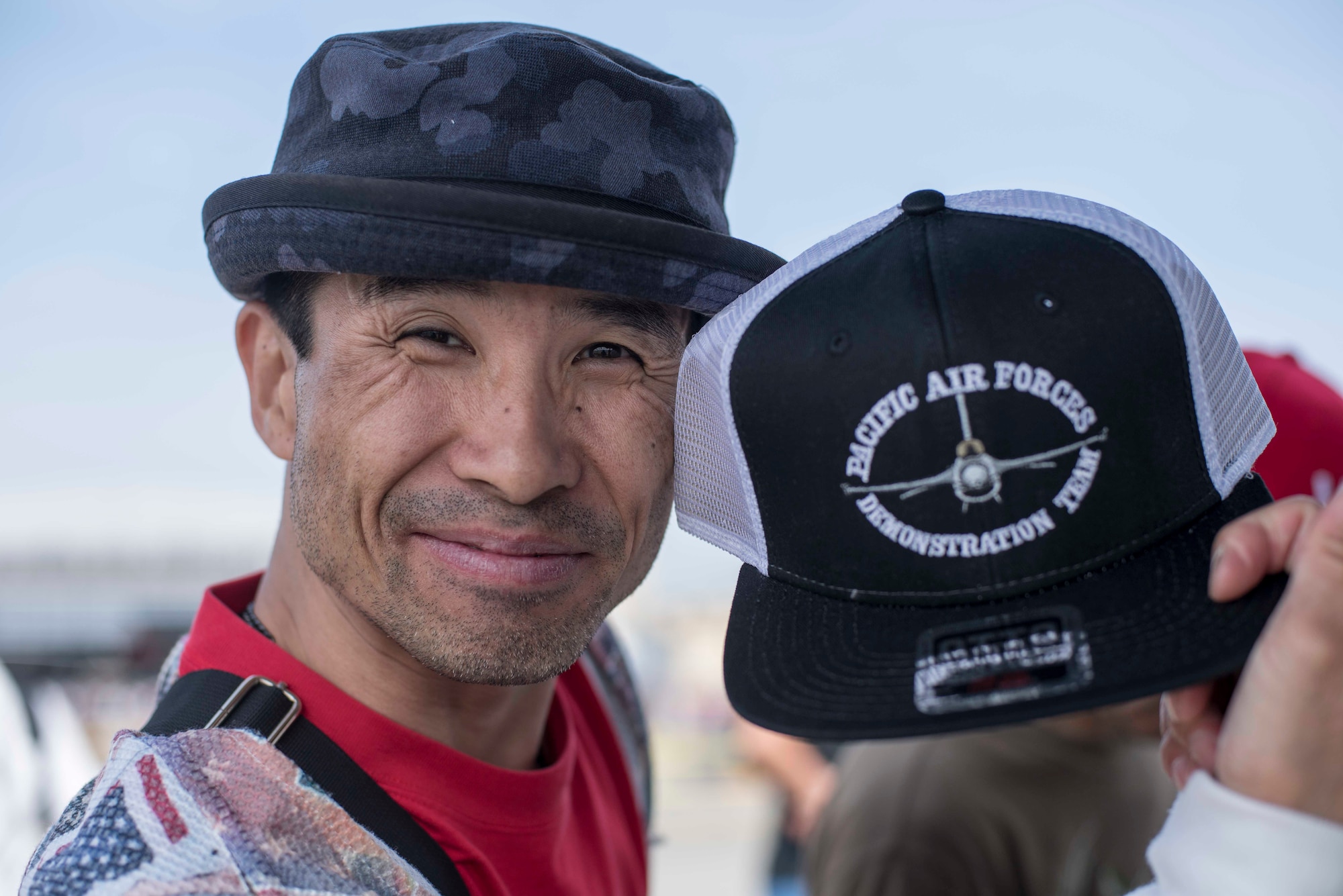 A 43rd Japan Maritime Self-Defense Force – Marine Corps Air Station Iwakuni Friendship Day 2019 guest holds a Pacific Air Forces Demonstration Team hat at MCAS Iwakuni, May 5, 2019. Attendees could purchase mementoes and souvenirs during the show. These items gave event spectators a way to promote and display their support for the PACAF F-16 Demo Team. (U.S. Air Force photo by Senior Airman Collette Brooks)
