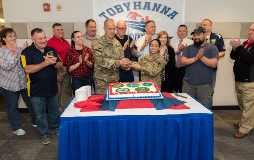 Depot employees stand watching the cake being cut with a sword.