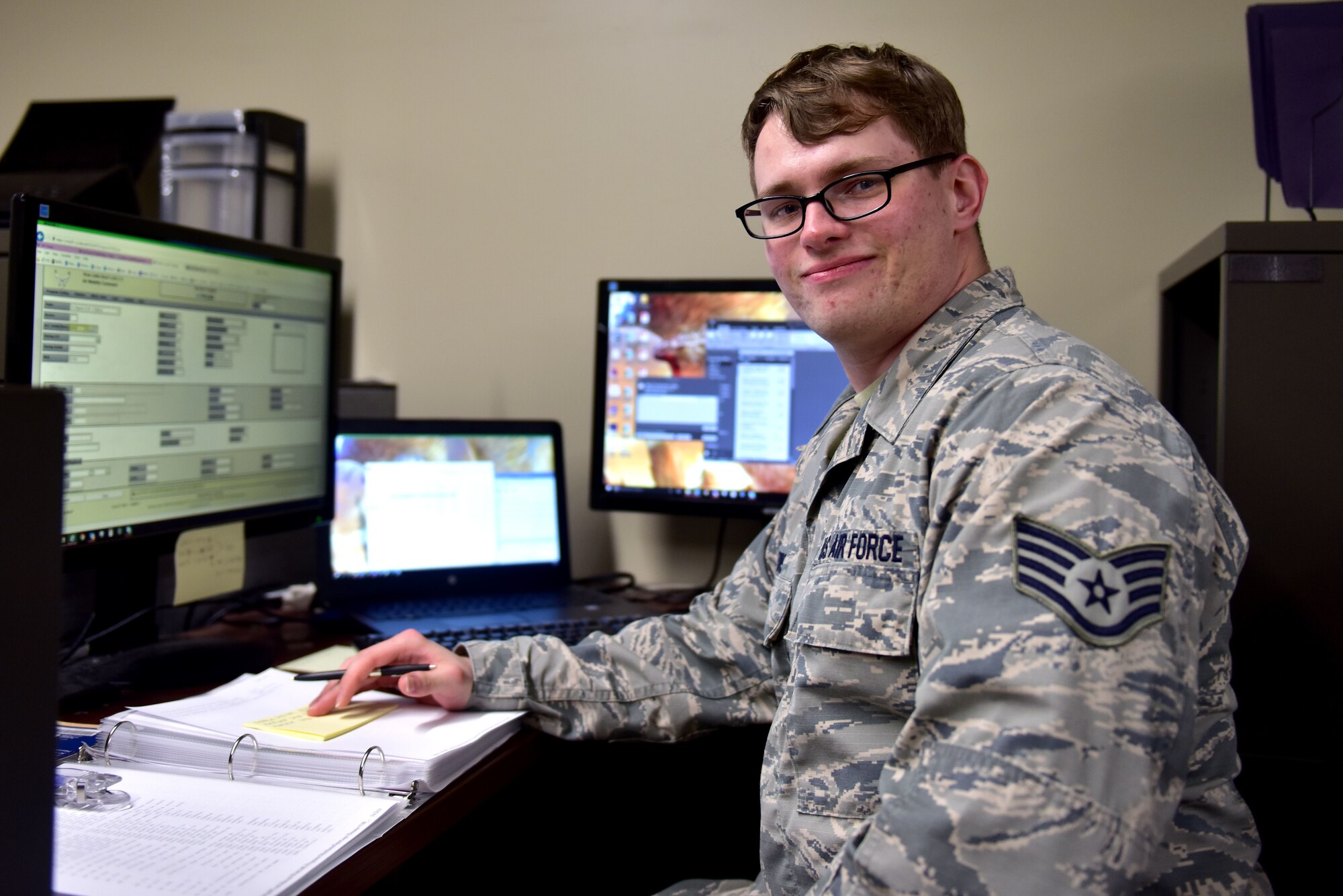 A man wearing the Airman Battle Uniform sits at a desk.