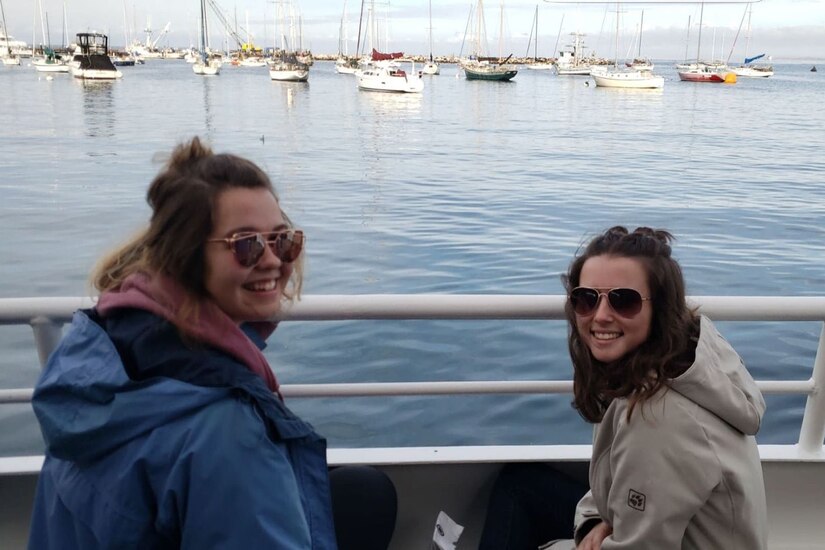 Two women in sunglasses sit on a bench in a marina.