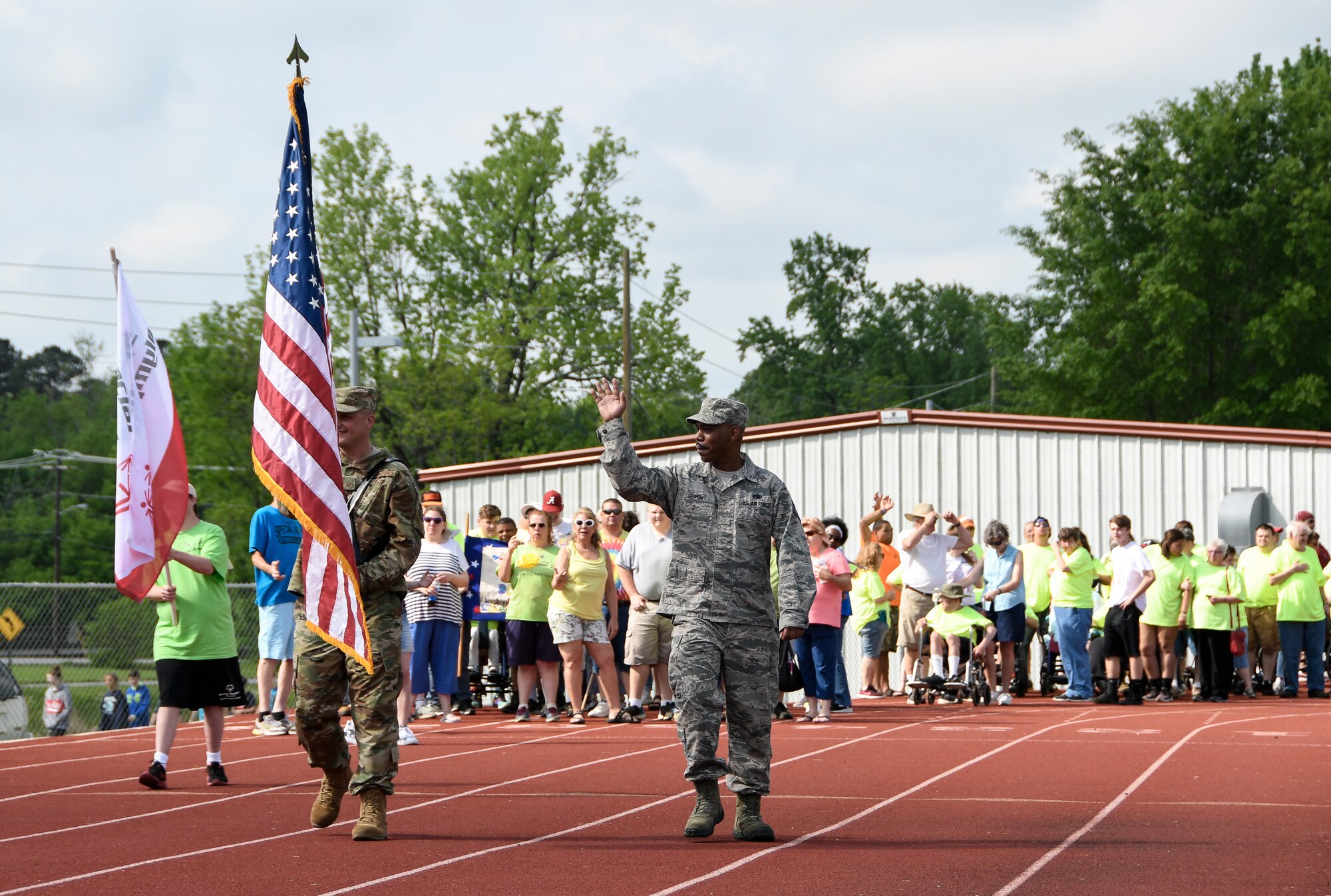 AEDC team member Master Sgt. Matt Krueger carries the U.S. flag as fellow team member Technical Sgt. Richard Griffin waves, both stationed at Arnold Air Force Base, to lead the parade of the opening ceremonies of the Tennessee Area 13 Special Olympics Spring Games May 2, 2019 at Tullahoma High School. (U.S. Air Force photo by Jill Pickett)