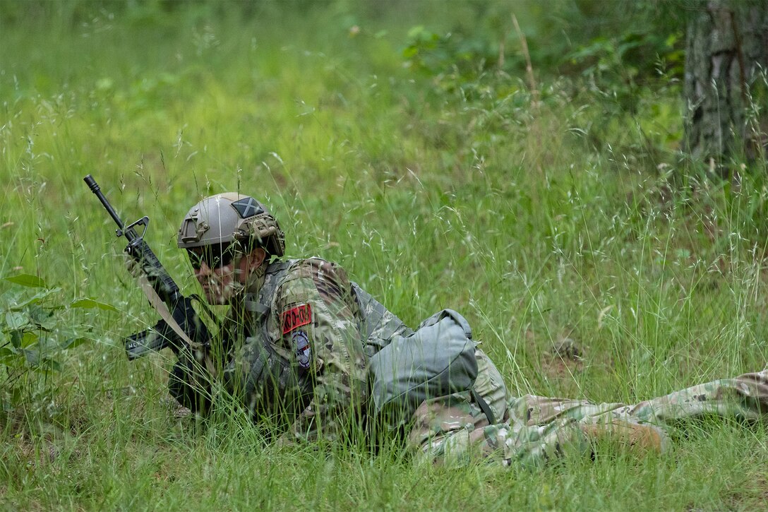 A soldier lays low in the grass during a competition.