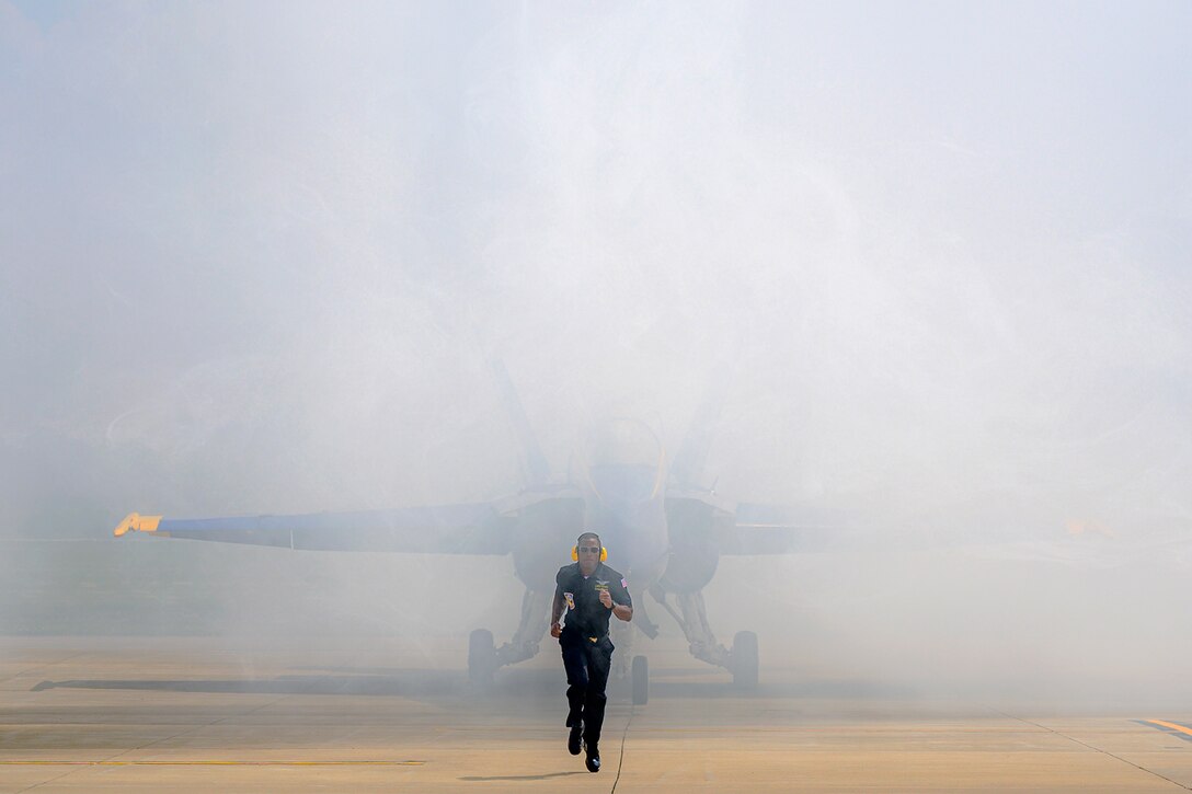 A sailor runs ahead of an aircraft on a runway before an air show.