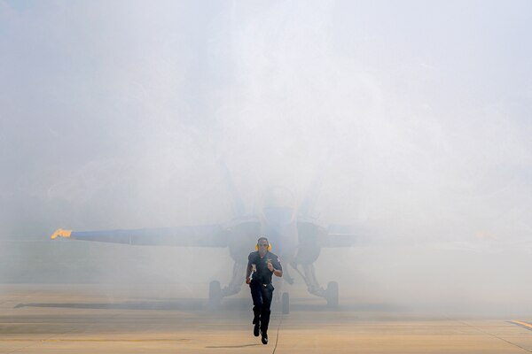 A sailor runs ahead of an aircraft on a runway before an air show.