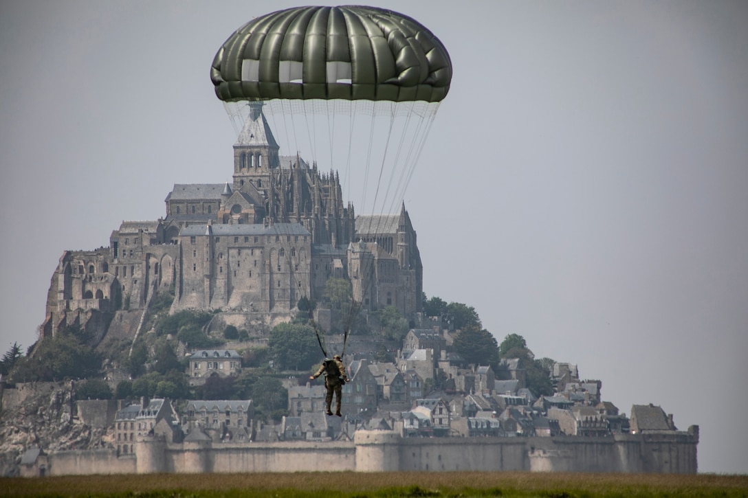 A soldier attached to a parachute descends in front of a giant fortress.