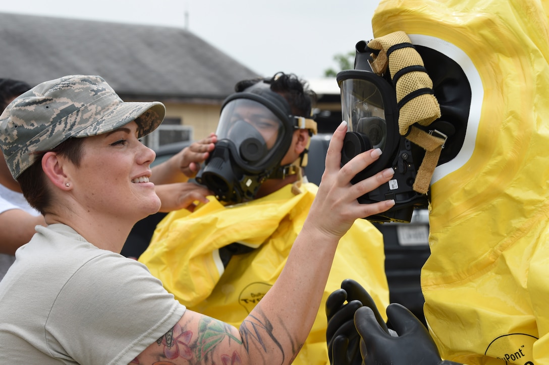 An airman places a hand over the mask of another airman in a hazmat suit.