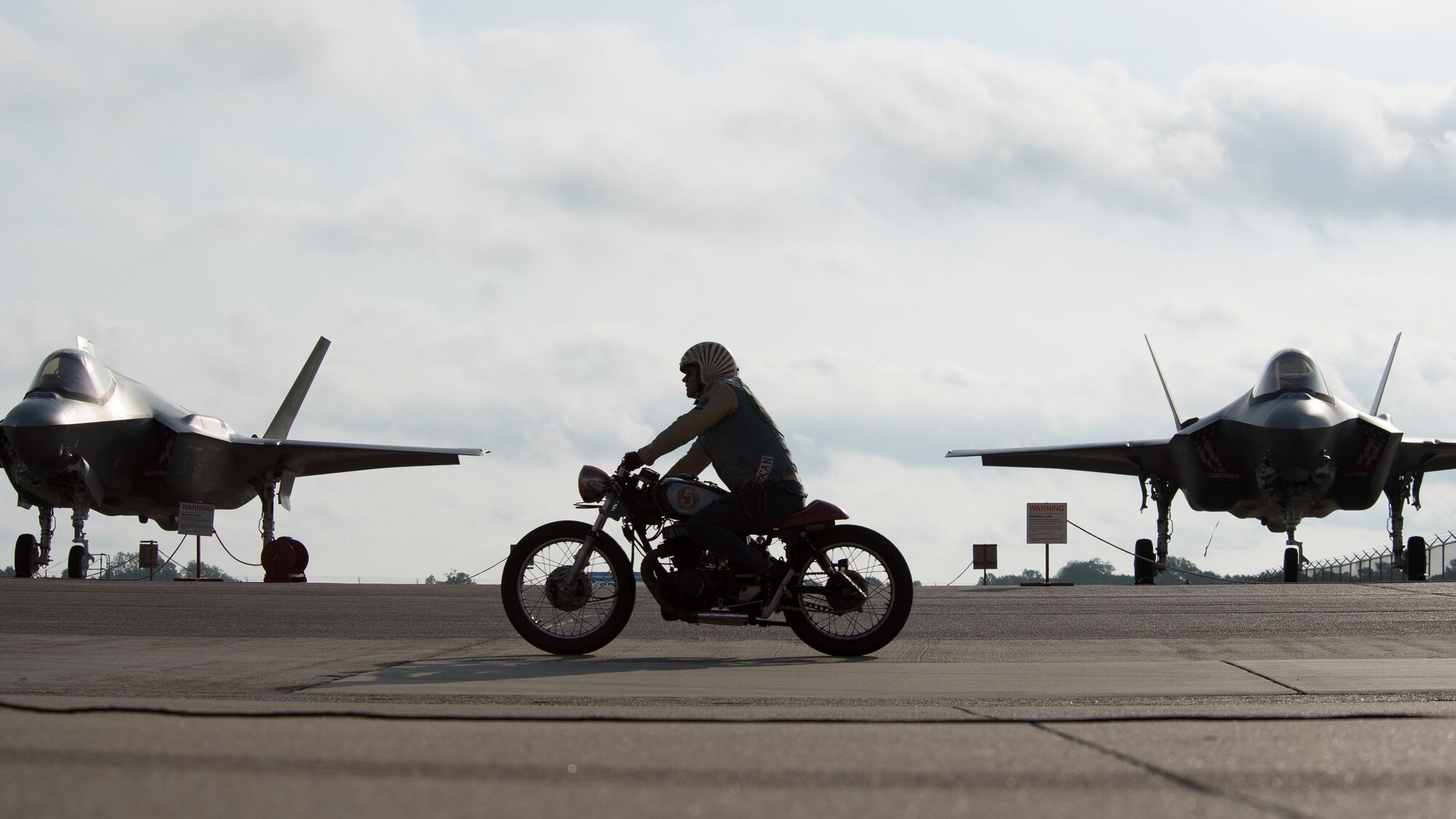A motorcycle rider drives in front of F-35A Lightning IIs as part of a Green Knight event before the Defenders of Liberty Air & Space Show at Barksdale Air Force Base, La., May 18, 2019. The airshow was first held in 1933 and is a full weekend of military and civilian aircraft and performances and displays. (U.S. Air Force photo by Staff Sgt. Damon Kasberg)
