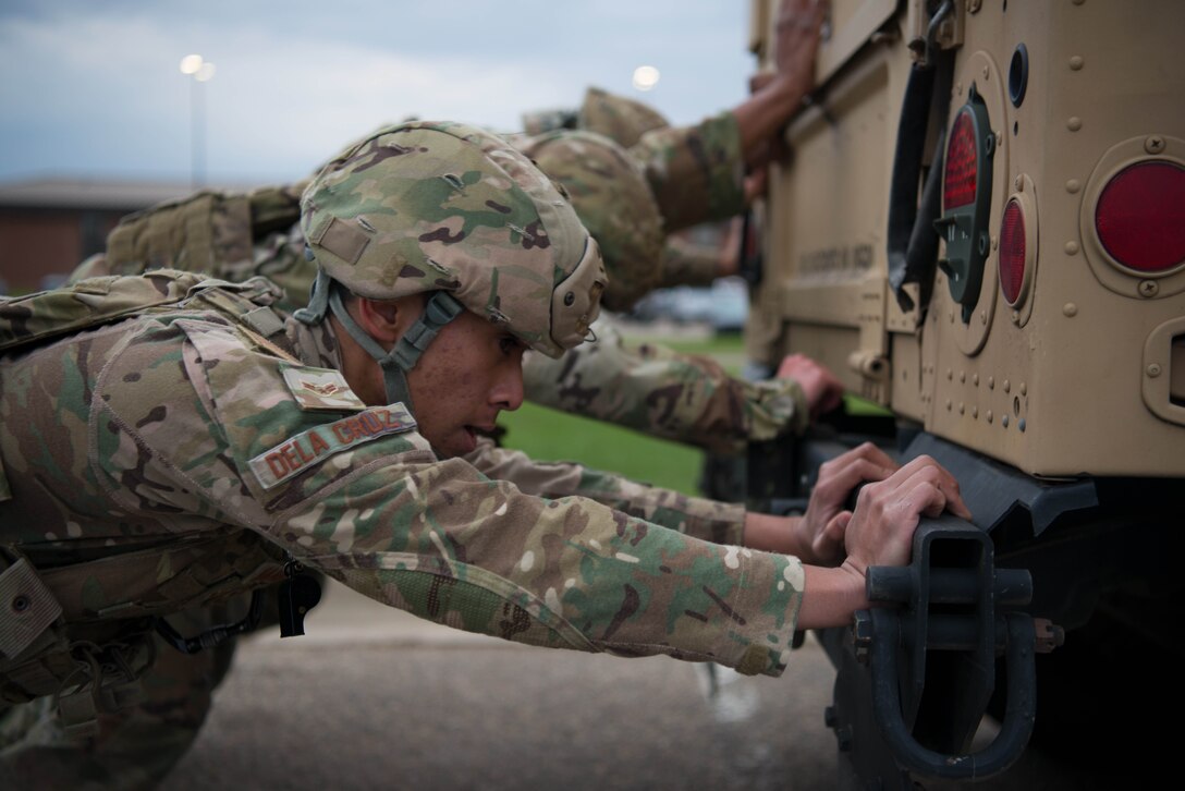 Four airmen in uniforms and helmets push on the rear of a Humvee.