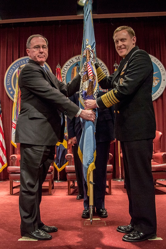 ADM Michael Rogers, USN, accepts the NSA flag from Dr. Michael Vickers, USDI, as he assumes responsibility for NSA, 03 April 2014