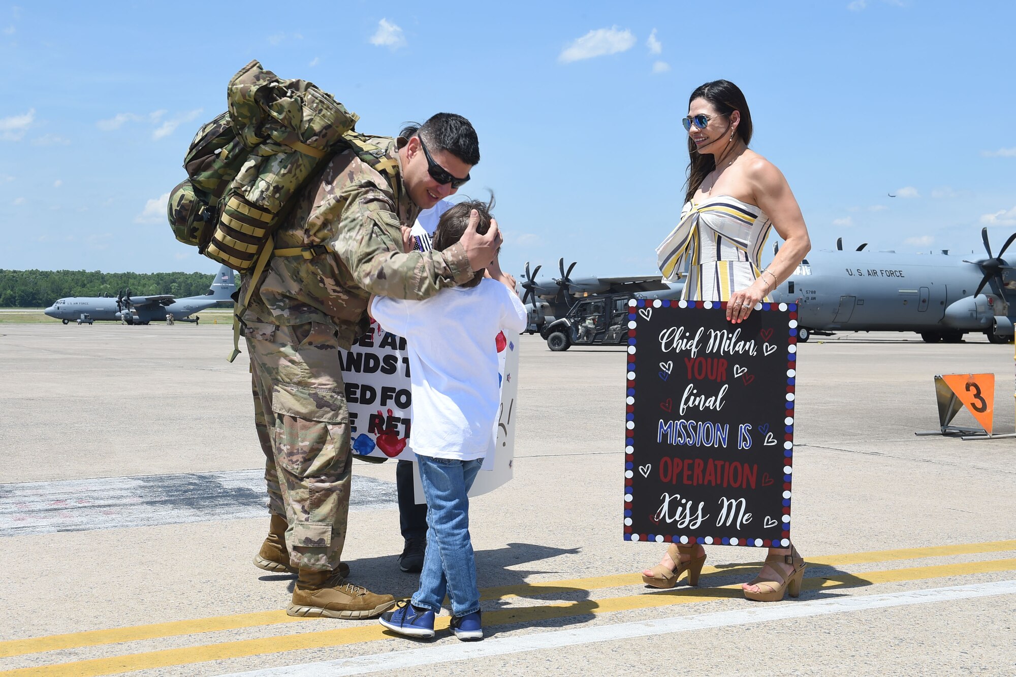 An Airman hugs his son while his wife looks upon them on the flight line