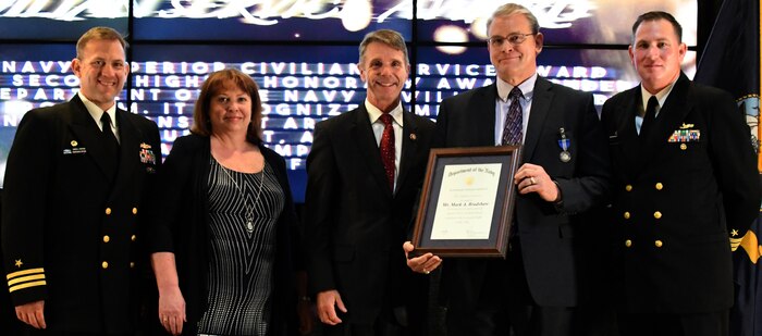 IMAGE: Mark Bradshaw receives the Navy Superior Civilian Service Award during the NSWCDD annual honorary awards ceremony, May 10. Standing left to right: NSWCDD Dam Neck Activity Commanding Officer Cmdr. Andrew Hoffman; NSWCDD Deputy Technical Director Angela Beach; U.S. Rep. Rob Wittman; Bradshaw; and NSWCDD Commanding Officer Cmdr. Stephen ‘Casey’ Plew.