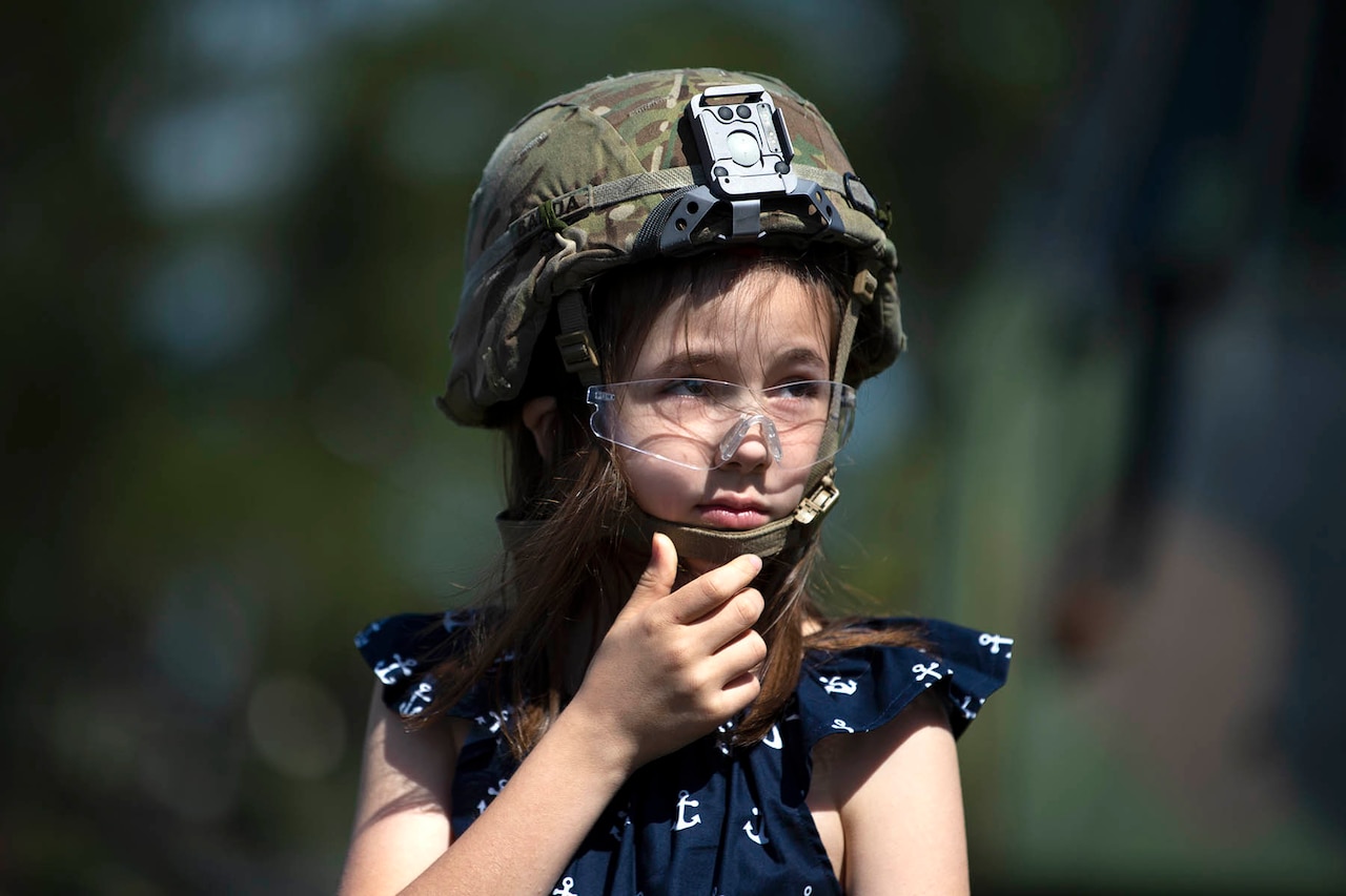 A girl wears a soldier’s helmet and safety goggles.