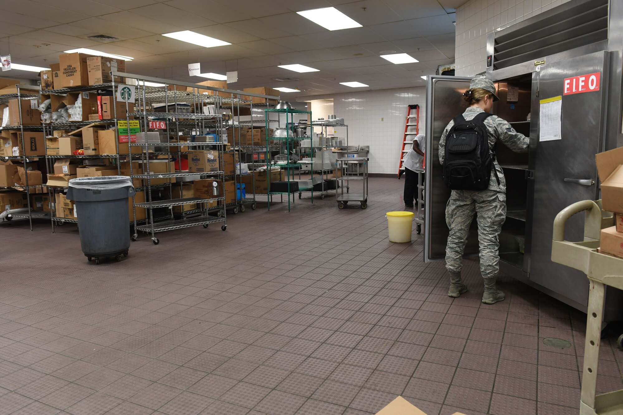 A woman stands in front of an open food container on the right side of the photo.