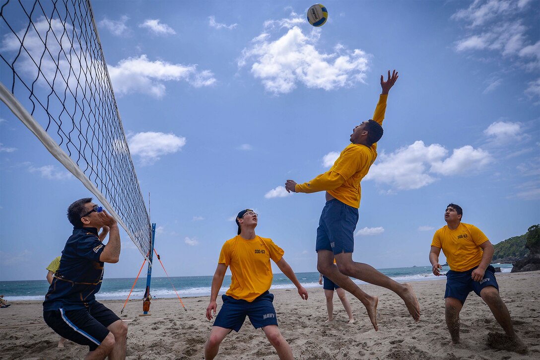 Sailors prepare to hit a volleyball at the beach.