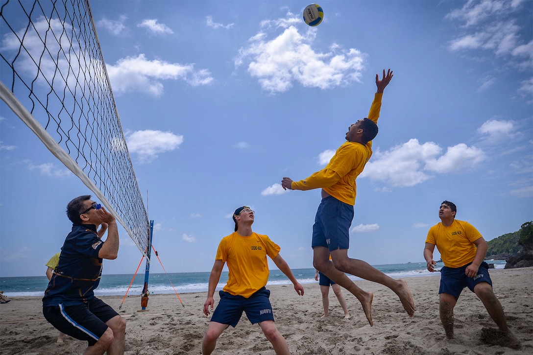 Sailors prepare to hit a volleyball at the beach.