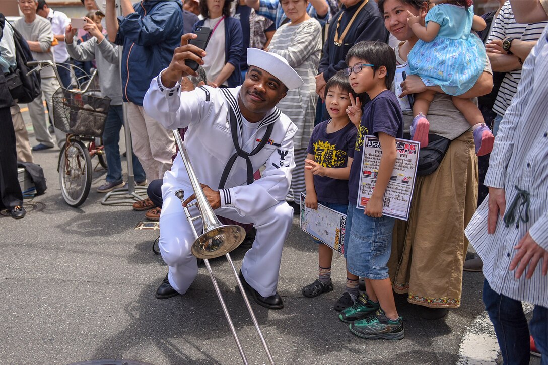 A sailor takes a picture with children during a festival.