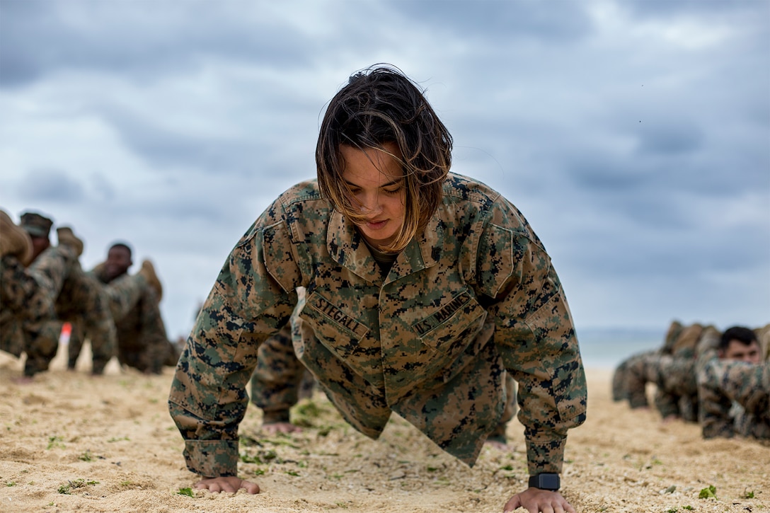A Marine does pushups in the sand with other Marines.