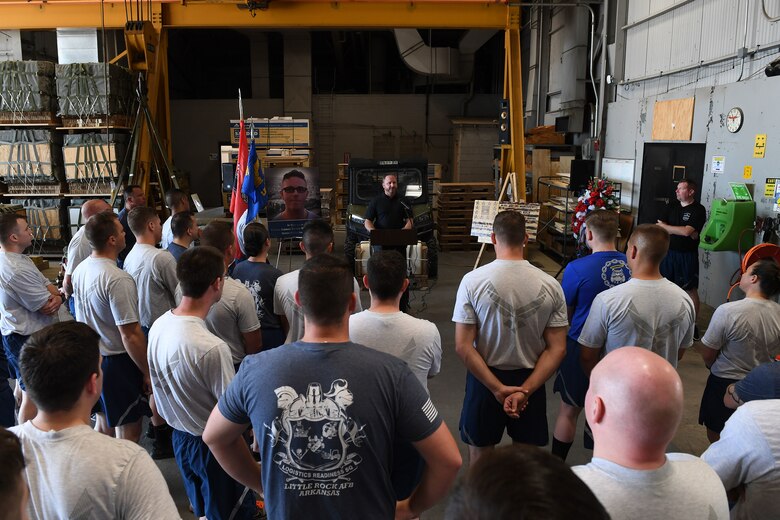 Airmen stand in front of a man speaking.