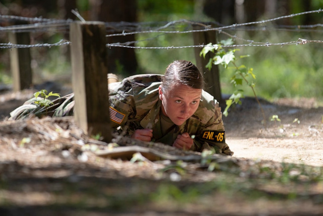 A soldier crawls under barbed wire.