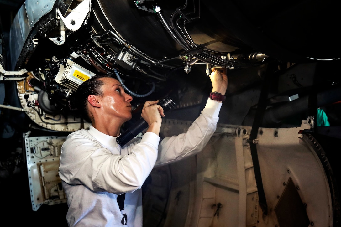 A sailor inspects the electrical system on an aircraft.