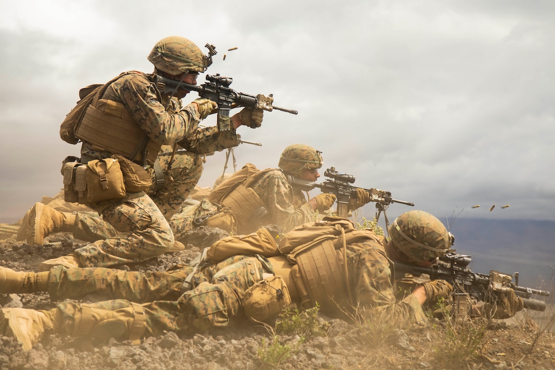 A Marine fire team fires rifles downrange from the ground.