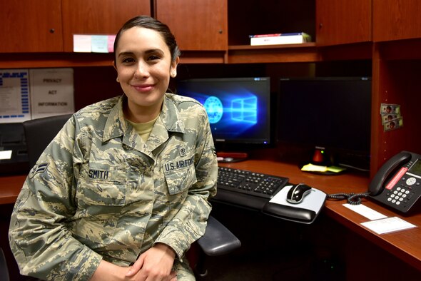 A woman wearing the Airman Battle Uniform sits at a desk.