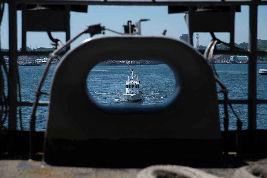 A boat  moves through water; seen through a hole in in a ship wall.