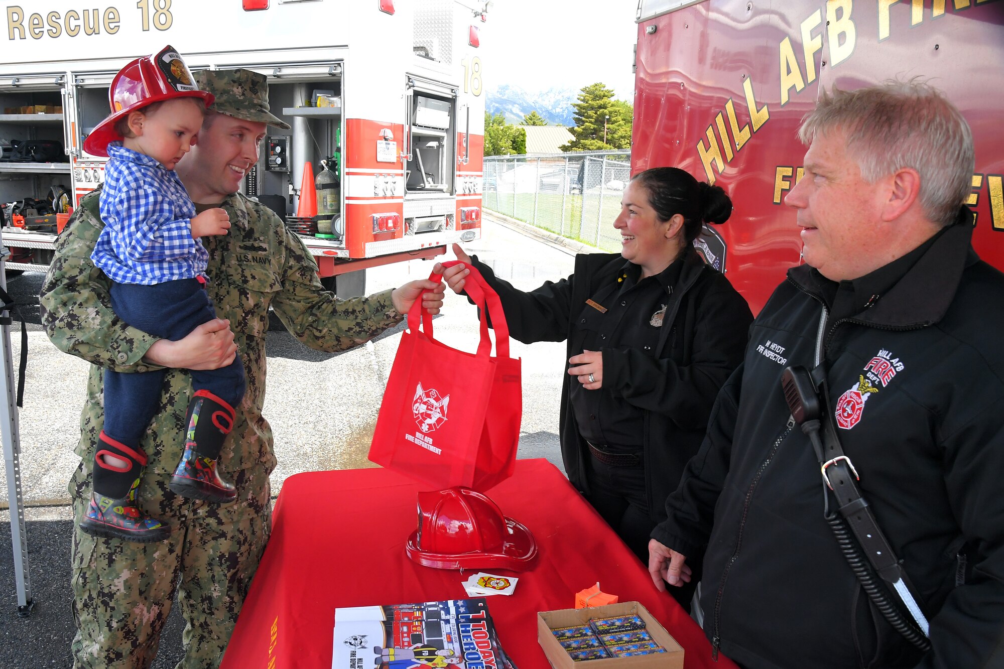 (left to right) Warren and Petty Officer 1st Class Gabe Burns, stop by to look at the Fire Trucks, and receive a child fire fighter helmet and other goodies from Tiana Bykowski and Wolfgang Heydt, both with 775 Civil Engineering Squadron, at the Wheels of Wonder event, May 17, 2019, Hill Air Force Base, Utah. (U.S. Air Force photo by Todd Cromar)
