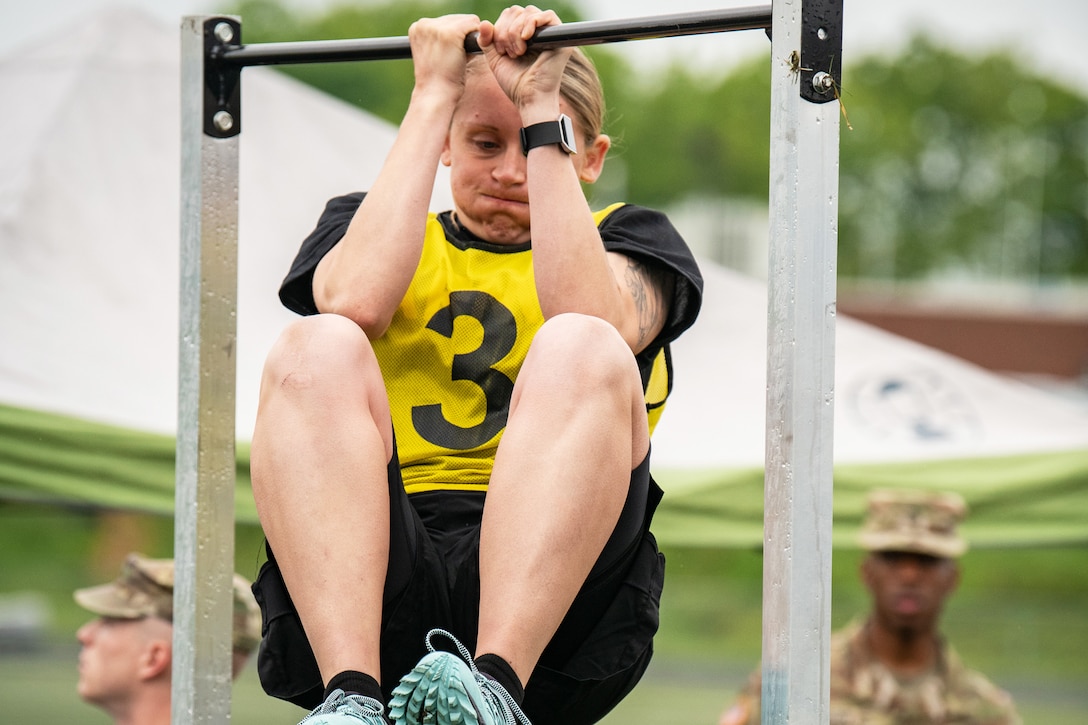 A soldier exhales while holding a chin-up bar and bringing her knees up.